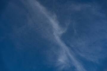 Fototapeta premium Wispy cirrus streaks cross deep blue sky; a minimal skyscape with smooth gradients and airy texture, ideal as clean background, weather concept or lifestyle design with selective focus.