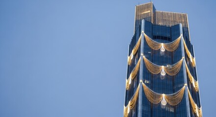 Modern high rise building decorated with festive golden garland lights against a clear blue sky. Winter holiday season architecture.