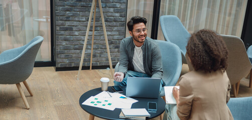 two founders reviewing charts and laptop over coffee, analytical discussion with printouts and...