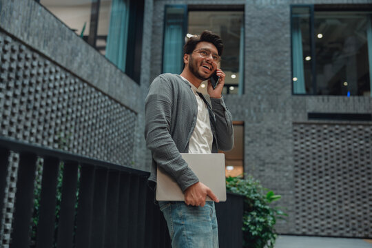 young professional on phone near staircase while carrying laptop, managing remote call and schedule