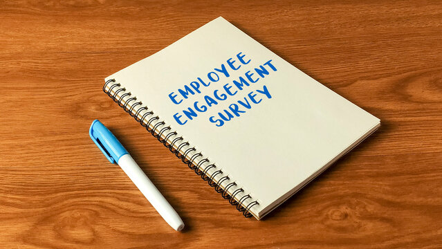 Employee Engagement Survey written on a spiral notebook with a marker on a wooden table for HR and workplace feedback.