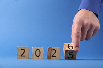 New Year. Man flipping cube with numbers 5 and 6 to make 2026 on blue background, closeup