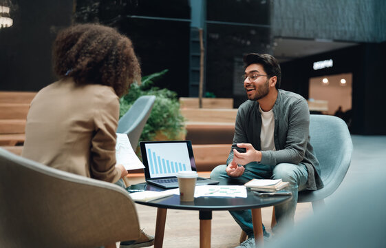 diverse team discussing charts over coffee with tablet and laptop, collaborative energy in open seating area,