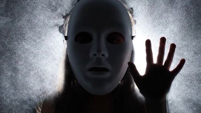 Mysterious Person in White Mask Pressing Hand Against Smoky Surface with Eerie Bright Light