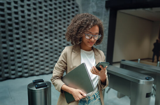 woman balancing laptop and phone near turnstile while checking access and schedule, showcasing efficient entry