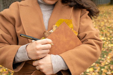 Woman holding a pen and a brown cover notebook