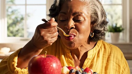 Senior woman at home savoring a spoonful of colorful fruit salad, embodying health, happiness, and a vibrant lifestyle while enjoying nutritious breakfast choices