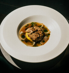 A white plate with a brownish food item in the center. The plate is round and has a greenish color