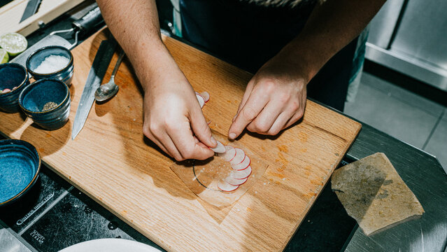 A person is preparing food on a wooden cutting board. The person is using a knife to cut vegetables