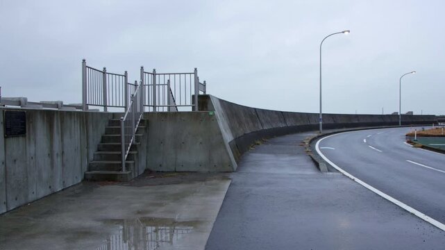 Seaside flood wall and empty curved road in Japan on cloudy day