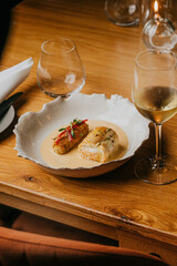 A plate of food with a glass of wine on a table. The plate has a fish and a vegetable dish, and the wine glass is filled with wine. The table setting is elegant and sophisticated, with a wooden table