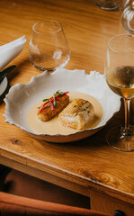 A plate of food with a white bowl and a glass of wine. The plate has a fish and a vegetable dish