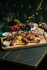 A tray of food with a glass of wine on a table. The food includes meat, potatoes, and vegetables. The wine glass is half full. Scene is festive and celebratory