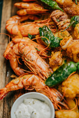 A plate of shrimp and other seafood is served on a wooden board. The shrimp are cooked and arranged in a way that makes them look appetizing. The plate also includes a dipping sauce