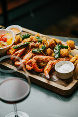A plate of shrimp and other seafood is on a wooden board. A glass of wine is next to the plate