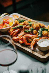 A plate of shrimp and vegetables is on a wooden board. A glass of wine is next to the plate