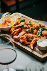 A plate of shrimp and vegetables is on a wooden board. A glass of wine is next to the plate