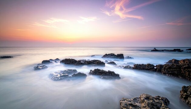 A tranquil coastal scene at sunrise with soft pastel colors in the sky and smooth, misty water flowing around dark rocks. - Powered by Adobe