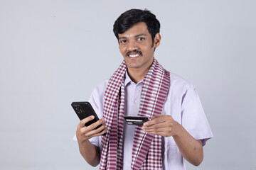 Indian young farmer using on mobile phone call by holding green credit card - concept of online payment on studio background