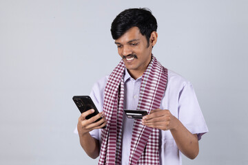 Indian young farmer using on mobile phone call by holding green credit card - concept of online payment on studio background
