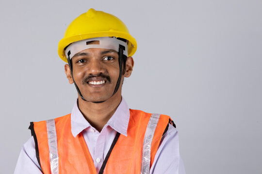 Close shot of a indian man engineer worker arm crossed and wearing safety uniform and yellow engineer cap. worker looking at camera isolated on studio grey background