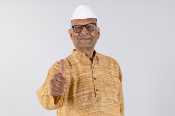 Indian happy senior Marathi man showing thumbs up while standing isolated on grey studio background
