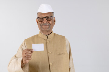 Portrait of  Indian senior politician Showing Aadhar card 
while wearing white cap on studio. Right to Vote