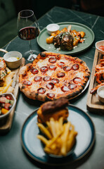 A table with a variety of food and drinks, including pizza, fries, and wine. The atmosphere is casual and inviting, perfect for a relaxed meal with friends or family