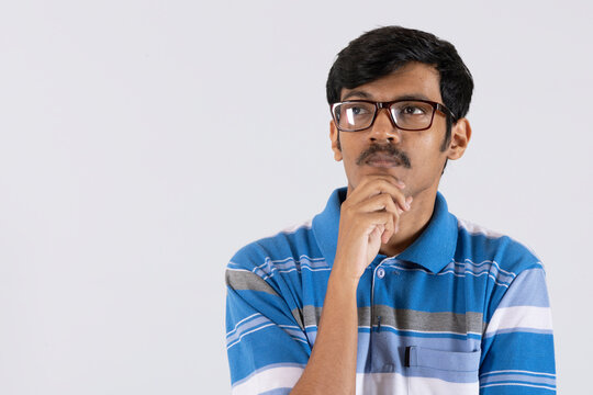 Portrait of a thoughtful Indian young man deep thinking, confused wearing eyewear isolated on white studio background 