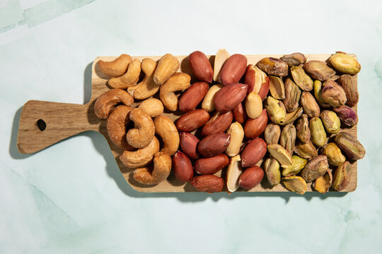 Top view of cashews, peanuts and pistachios on small wooden board.