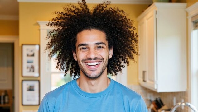 Portrait of a happy young man with curly hair smiling in a bright kitchen at home