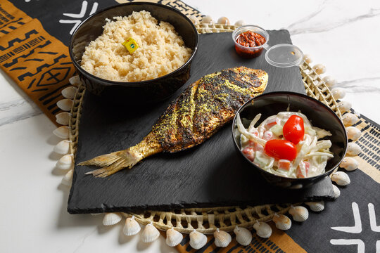 Atti&eacute;k&eacute; servi avec poisson brais&eacute;, semoule de pulpe de manioc ferment&eacute;e cuite &agrave; la vapeur, pr&eacute;sent&eacute; sur une ardoise et un set de table tiss&eacute; africain &ndash; plat traditionnel africain.
