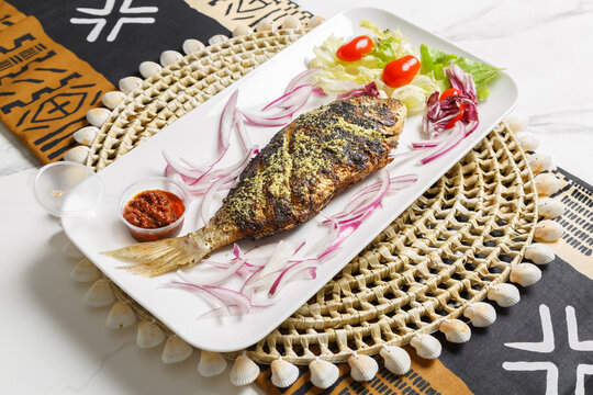 Poisson brais&eacute;, pr&eacute;sent&eacute; sur une ardoise et un set de table tiss&eacute; africain &ndash; plat traditionnel africain.