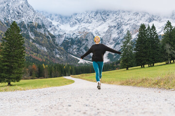 Young attractive woman hiking in nature. Beautiful happy girl stands on road looking at mountains view. Autumn or winter nature landscape. Photo of female having a walk with a backpack outdoors.