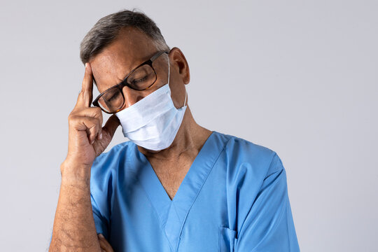 Portrait of a indian physiotherapist in light blue gown and face mask deep thinking isolated studio background. Protect yourself and others medical advice against the covid-19