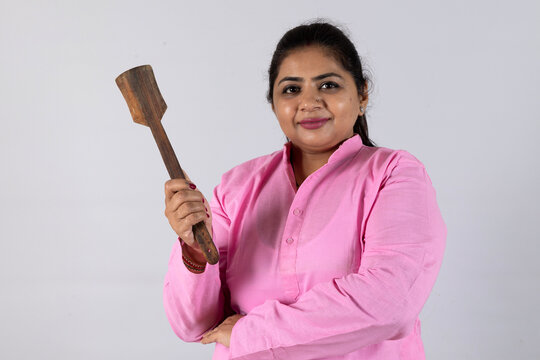 Indian smiling young woman holding wooden spatula. House wife showing kitchen items and home appliances products for cooking food. while standing isolated over white background