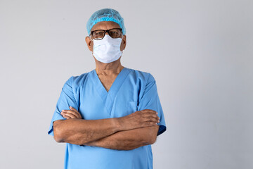 Portrait of a indian senior physiotherapist arm crossed in light blue gown and face mask deep thinking isolated studio background. Protect yourself and others medical advice against the covid-19