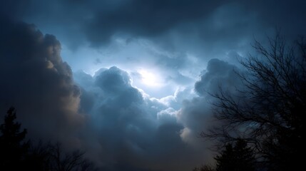 A dramatic sky with stormy dark clouds parting to reveal a bright luminous light source with silhouetted trees in the foreground