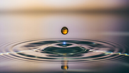 A macro photo of a golden liquid drop falling into water creating a splash and ripples. High-speed photography capturing the moment of impact with reflection.