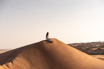 Woman sitting alone on desert sand dune in oman