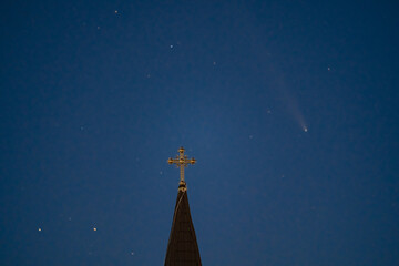 Celestial and Spiritual: Rare Comet ATLAS 2024 Shines Brightly in the Night Sky Behind the Illuminated Cross of an Old Wooden Church, Symbolizing Faith and Science