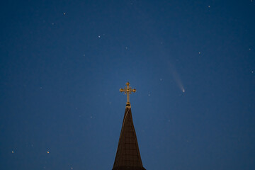 Celestial and Spiritual: Rare Comet ATLAS 2024 Shines Brightly in the Night Sky Behind the Illuminated Cross of an Old Wooden Church, Symbolizing Faith and Science