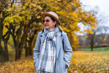 Beautiful middle-aged woman walking in park in autumn scenery. Front view	