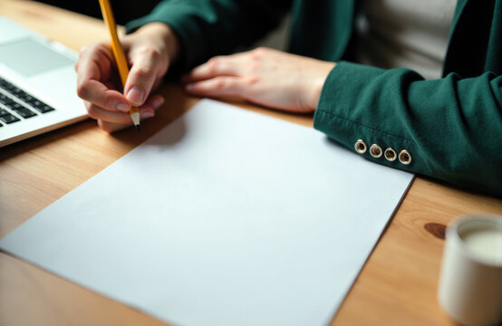Person writing on blank sheet of paper with a pencil in a workspace setting - Powered by Adobe