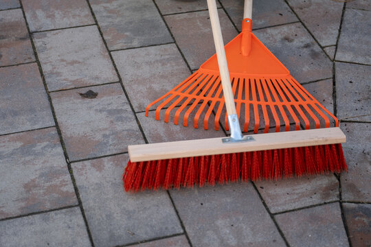 Bright orange garden tools on stone pavement rake and broom for outdoor maintenance