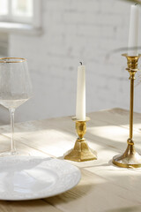 Elegant table setting with candle holders, white plate, and wine glass in natural sunlight