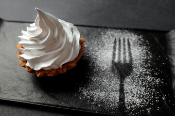 The sand basket is decorated with a high peak of protein cream. A tasty and sweet dessert stands on a black plate on a gray background