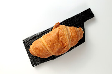 Crispy hot croissant on a black rectangular wooden board on a white background