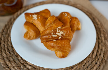 Flaky croissants on white plate. Minimal cozy breakfast with warm natural light and soft shadows. 
