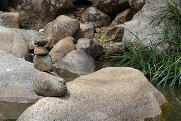 Balanced rock cairn on a large boulder by a peaceful forest stream, representing zen and tranquility. © Irina